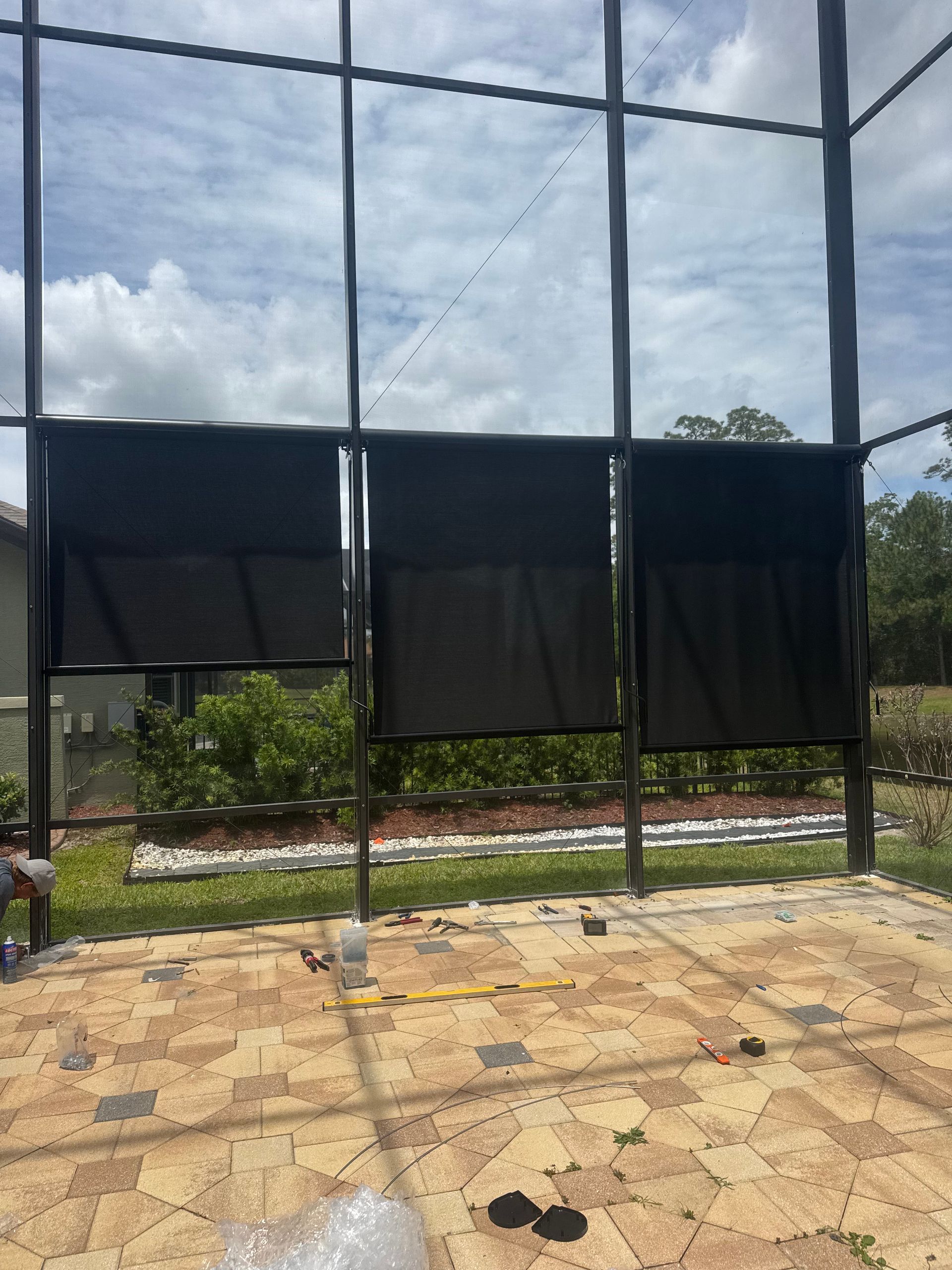 Black netted outdoor enclosure with three hanging panels over a tiled area and cloudy sky beyond
