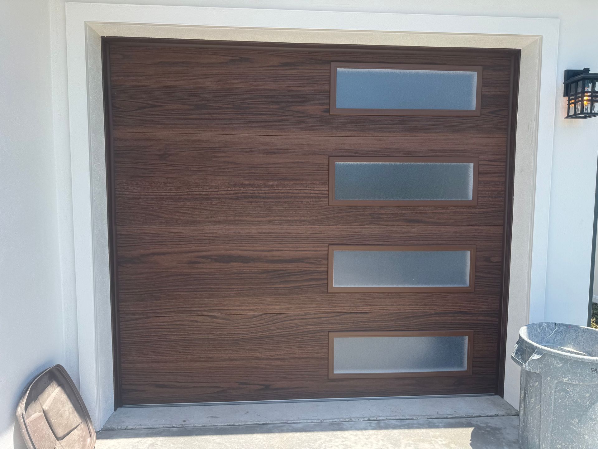 Modern wood garage door with four narrow frosted glass windows beside a stone driveway and white trim