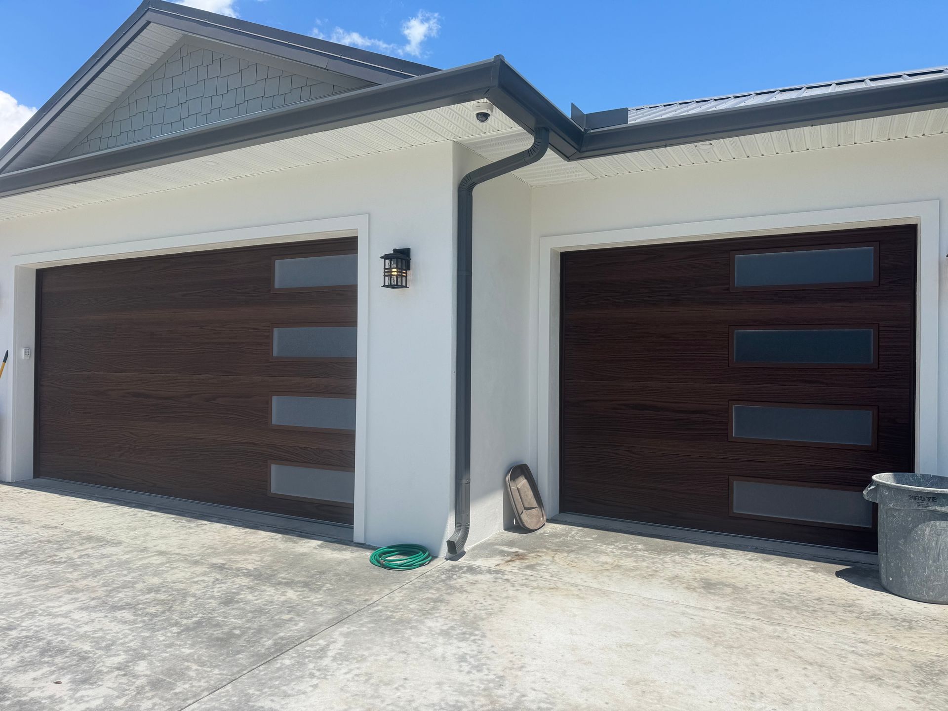 Two dark wood garage doors on a white suburban house under a bright blue sky