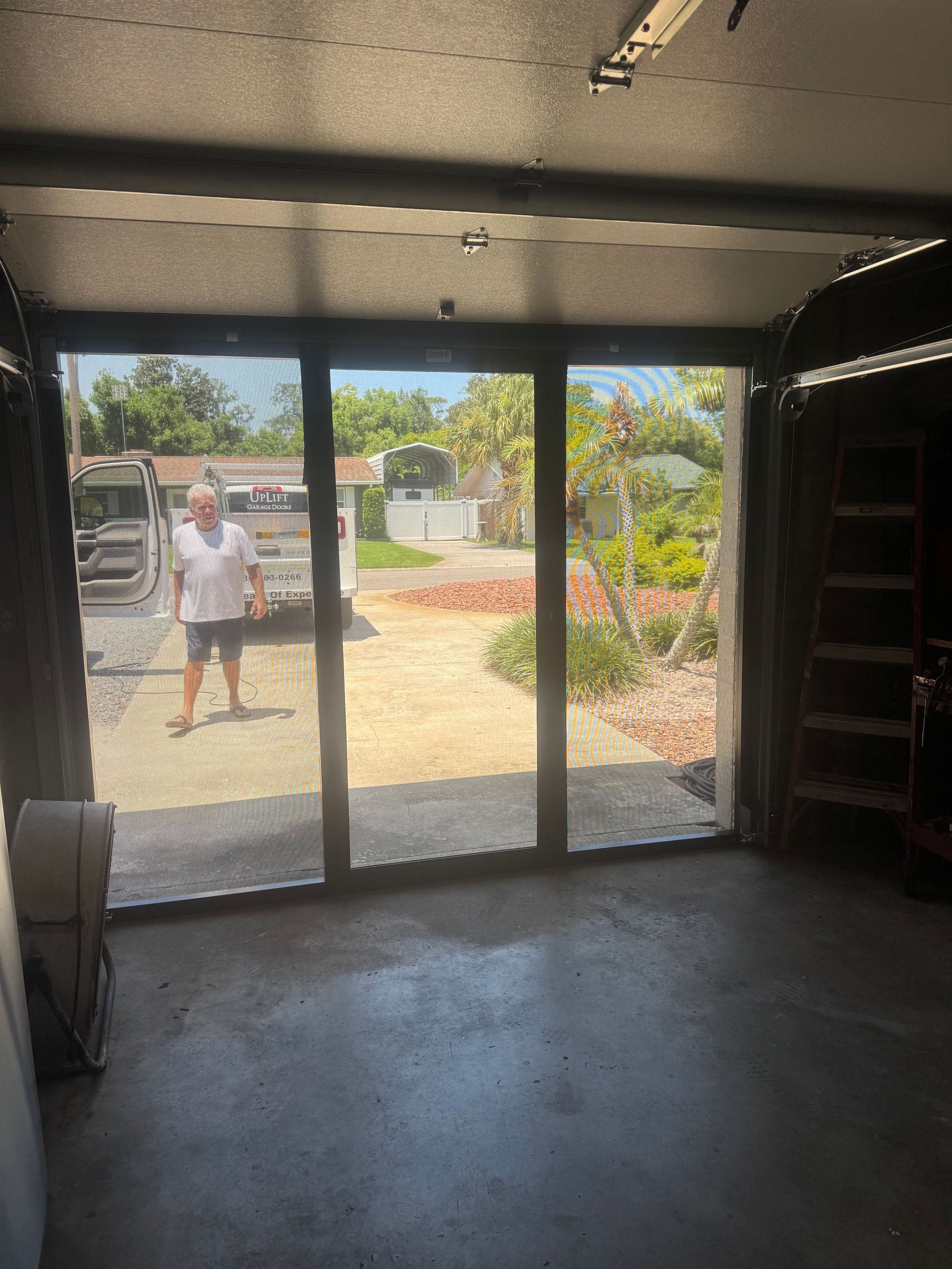 View from a dark interior through glass doors to a bright yard with a person standing outside