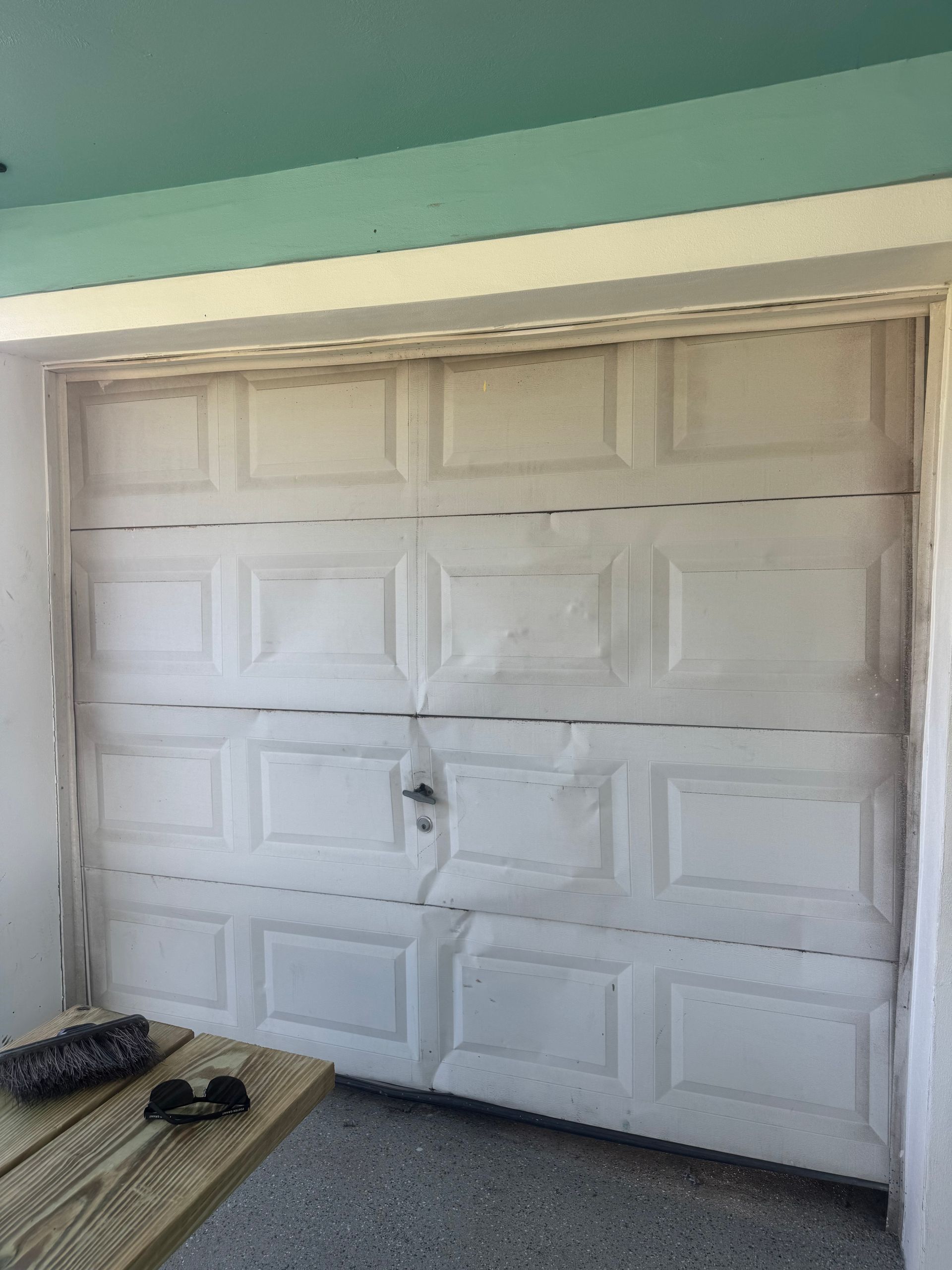 White garage door with rectangular panels and a small lock, viewed from a porch.