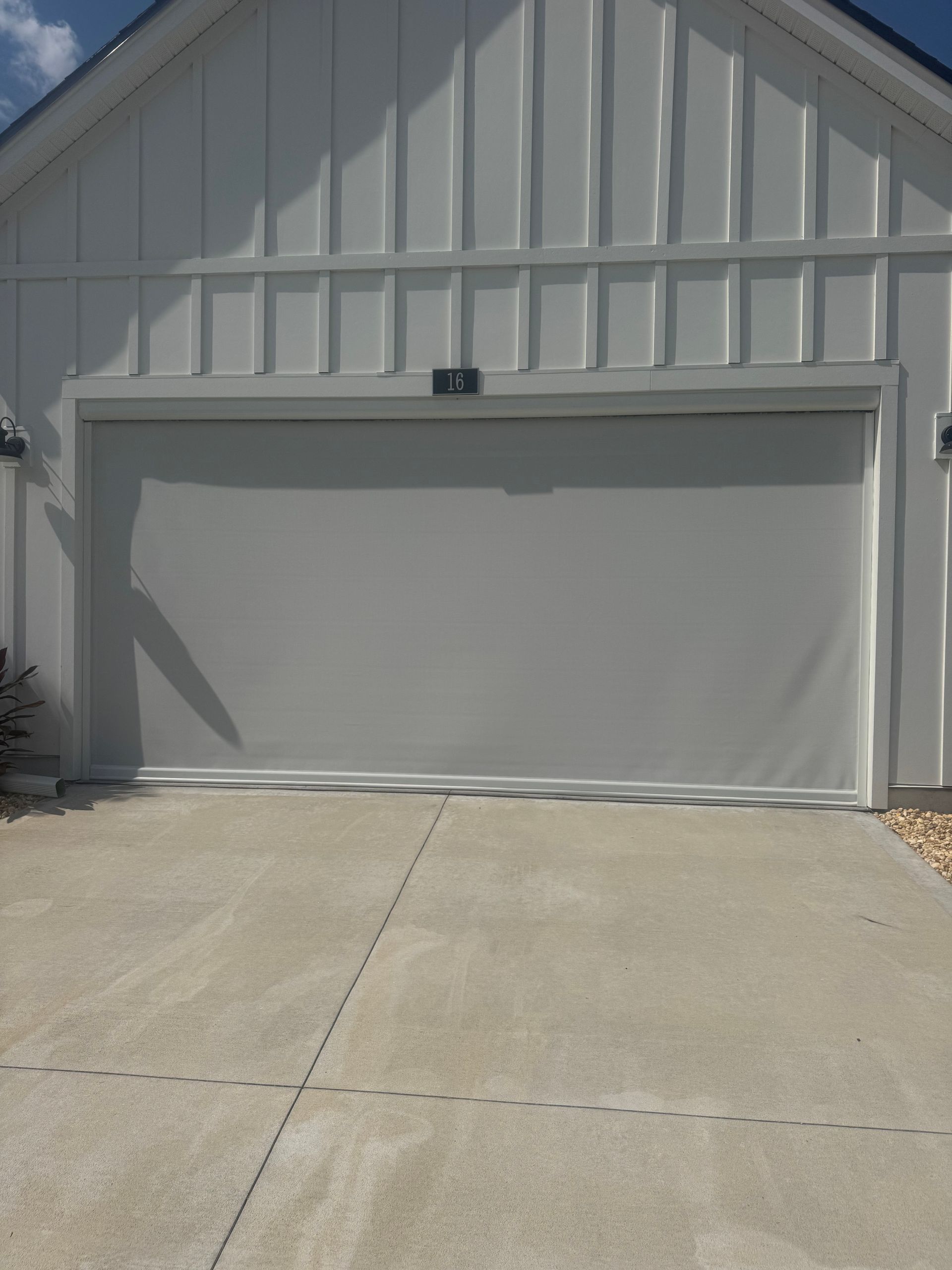 Closed white garage door on a light gray house with a concrete driveway