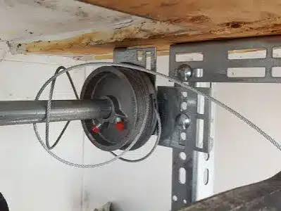 Garage door opener spring and cable assembly mounted on a metal bracket under a wooden beam