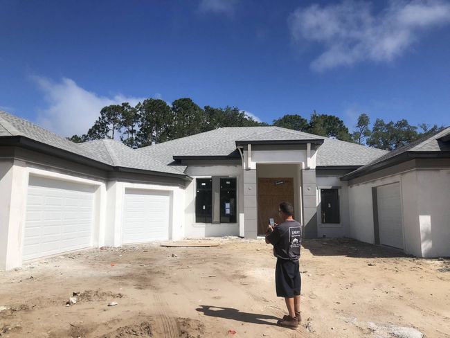 New house under construction with a person standing in the dirt driveway.