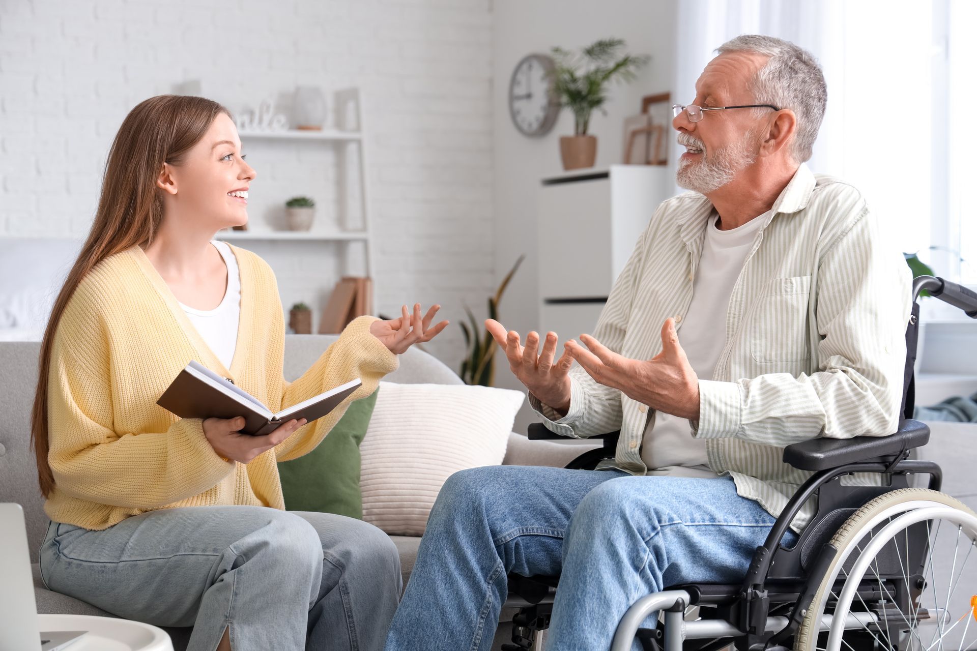 Woman talking with an older man in a wheelchair in a bright living room