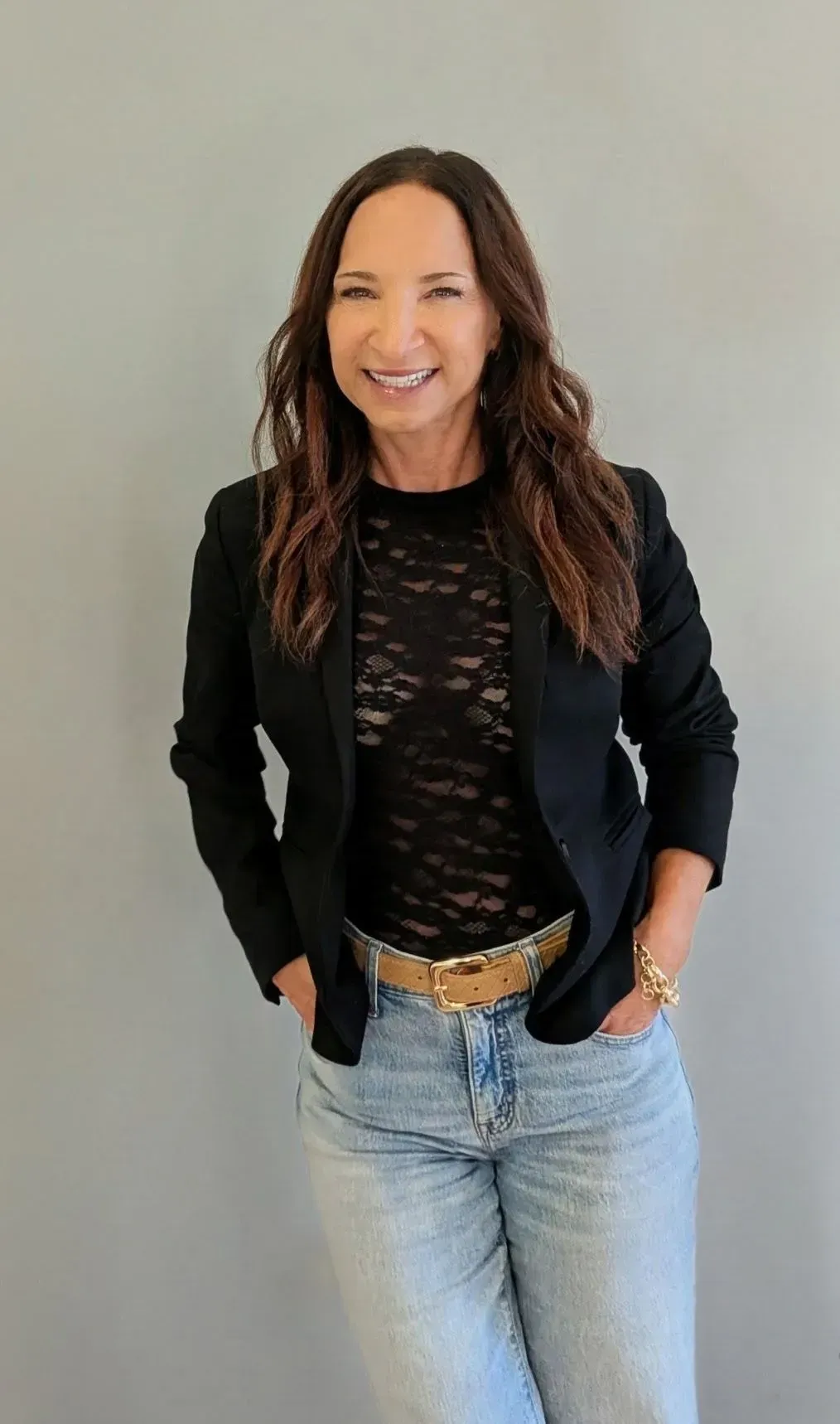 Amy standing against a gray background, wearing a black blazer, black top, and light blue jeans, smiling.