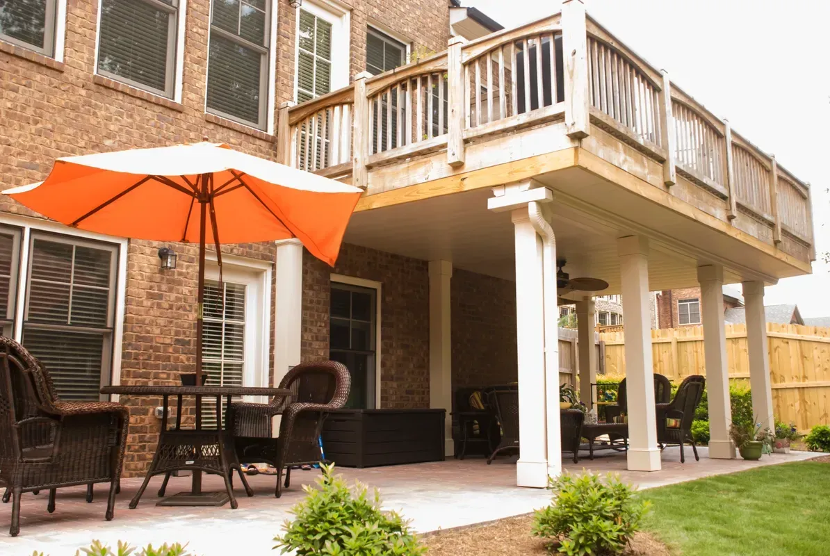 Back patio with orange umbrella, patio table and chairs, and a wooden deck above white columns