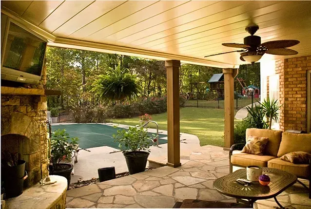 Covered patio with wicker chairs, ceiling fan, and pool view opening to a lush backyard