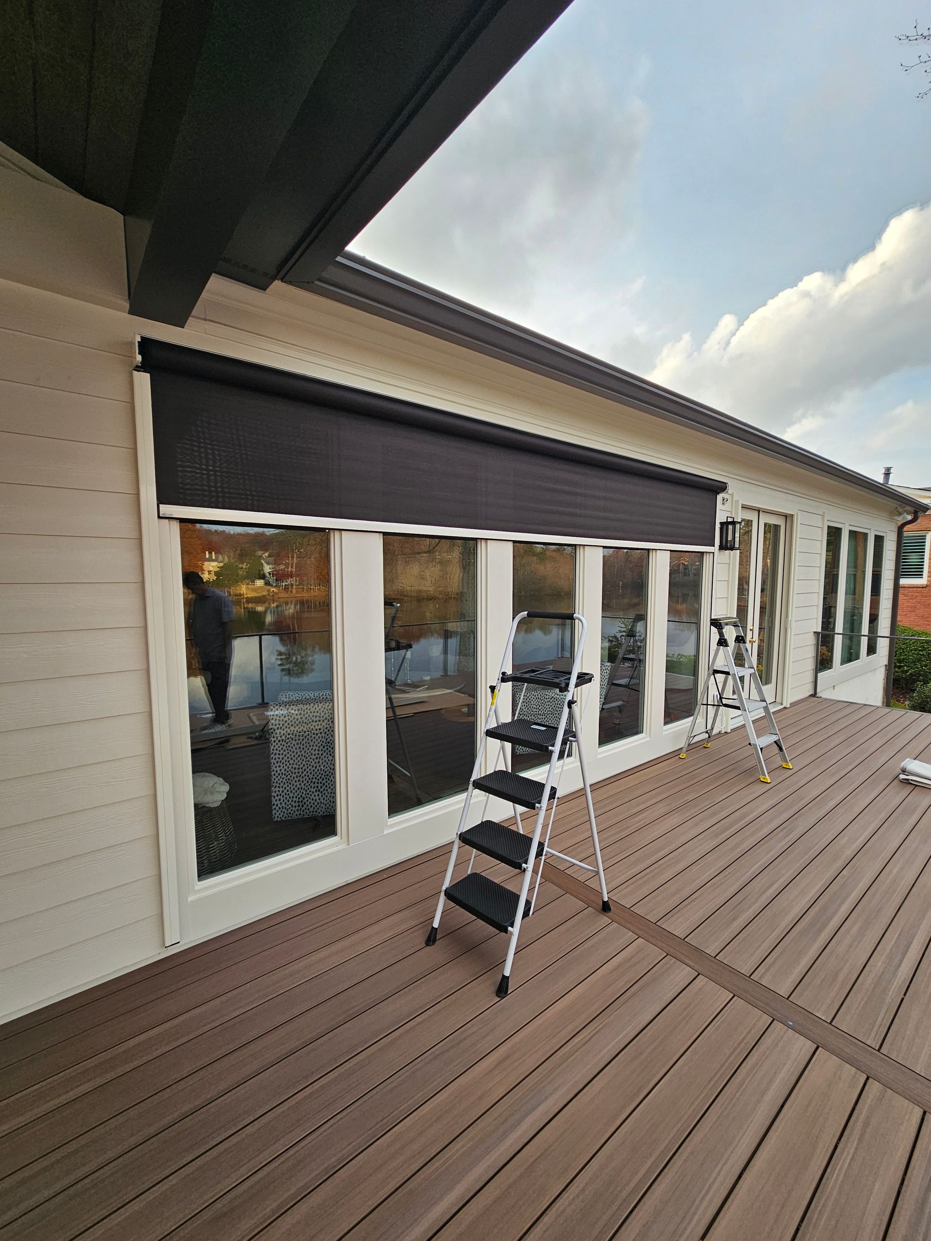 Deck with white house siding and windows, dark awning, and a step ladder on a wooden patio.