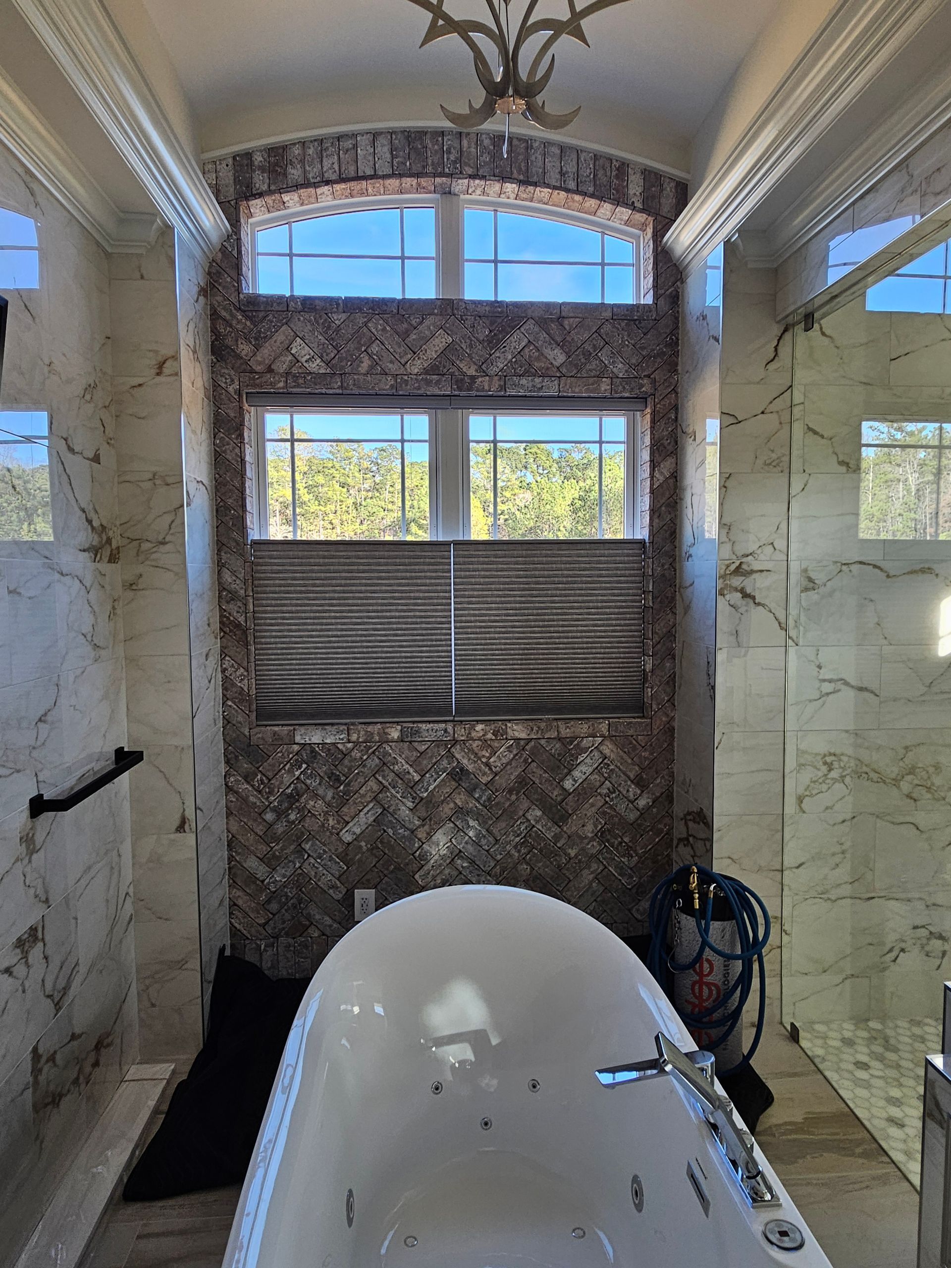 Marble bathroom with a freestanding tub facing a large window and ornate chandelier.
