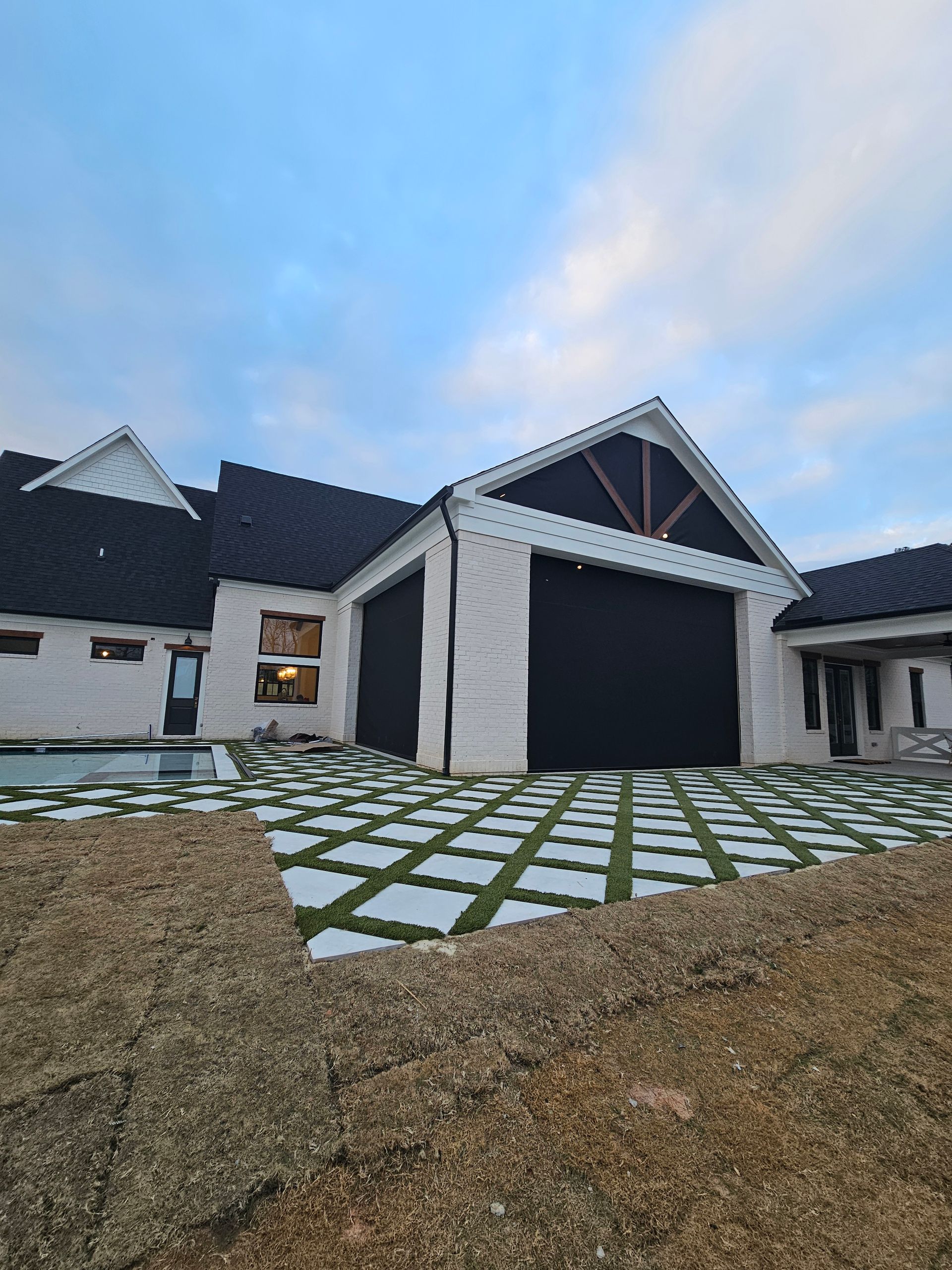 Modern house exterior with black roof, large garage, and stone paver driveway at dusk