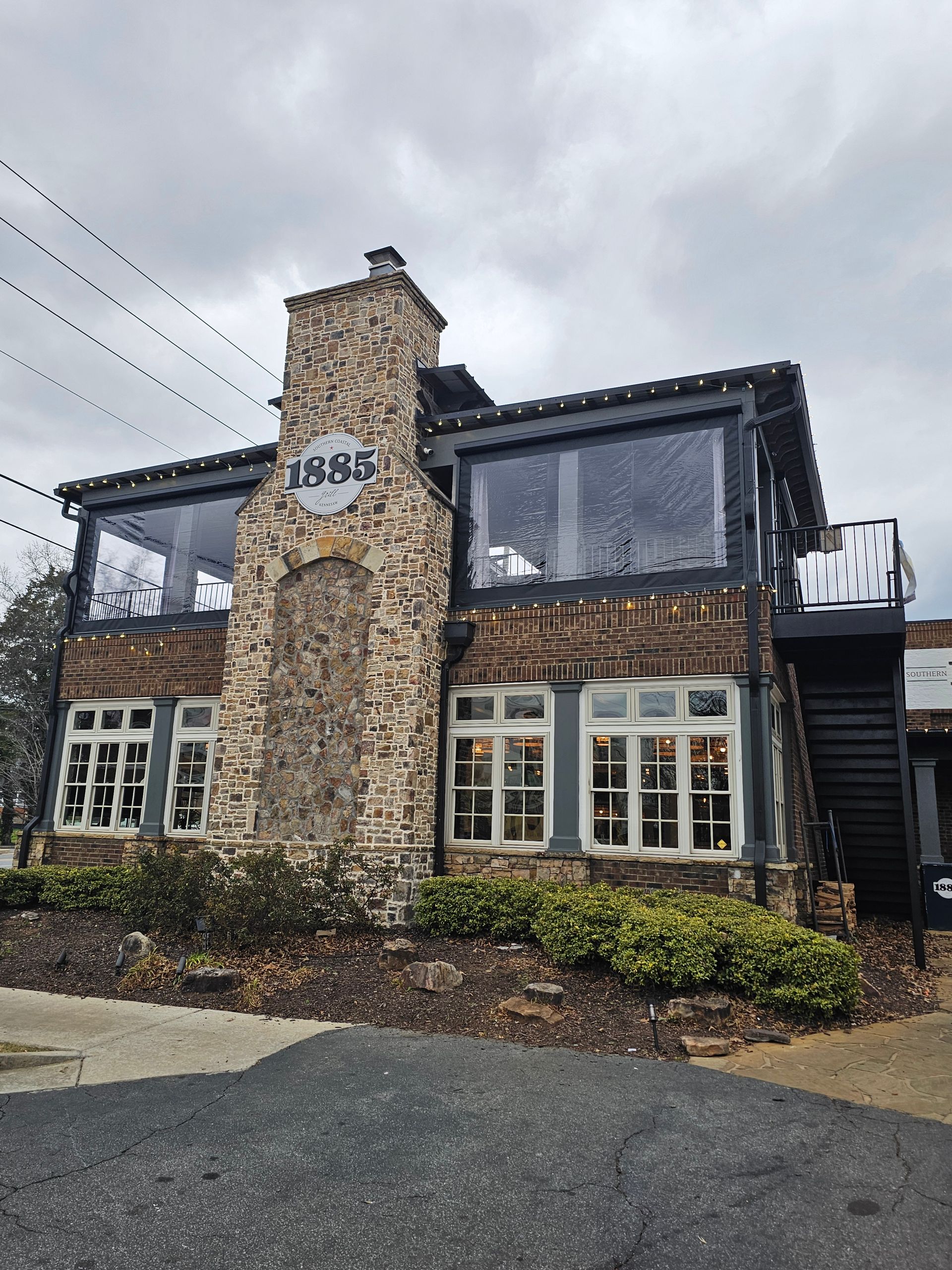 Two-story stone pub with black trim and large windows under a cloudy sky