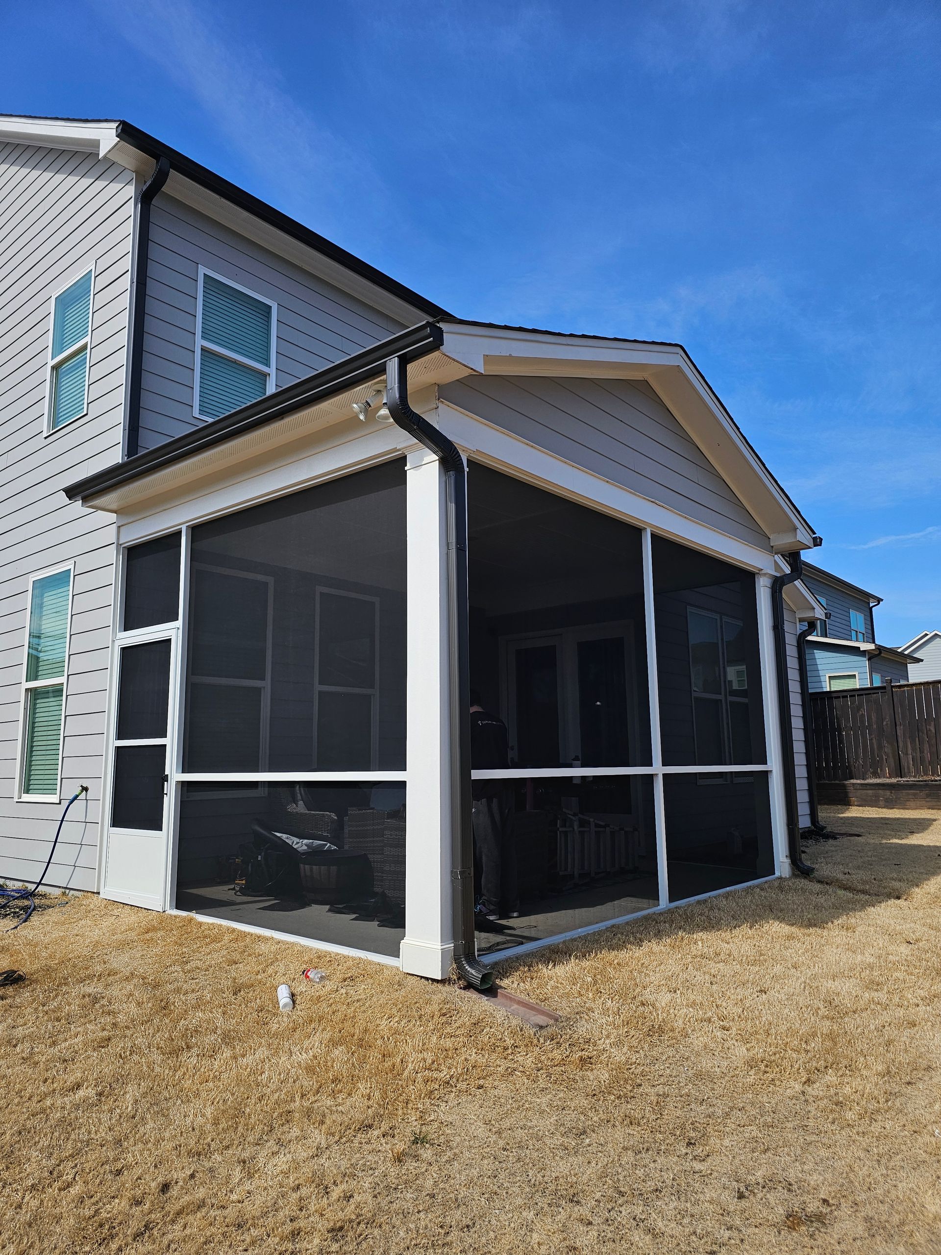Screened-in porch with white trim and dark mesh on a two-story house under a blue sky