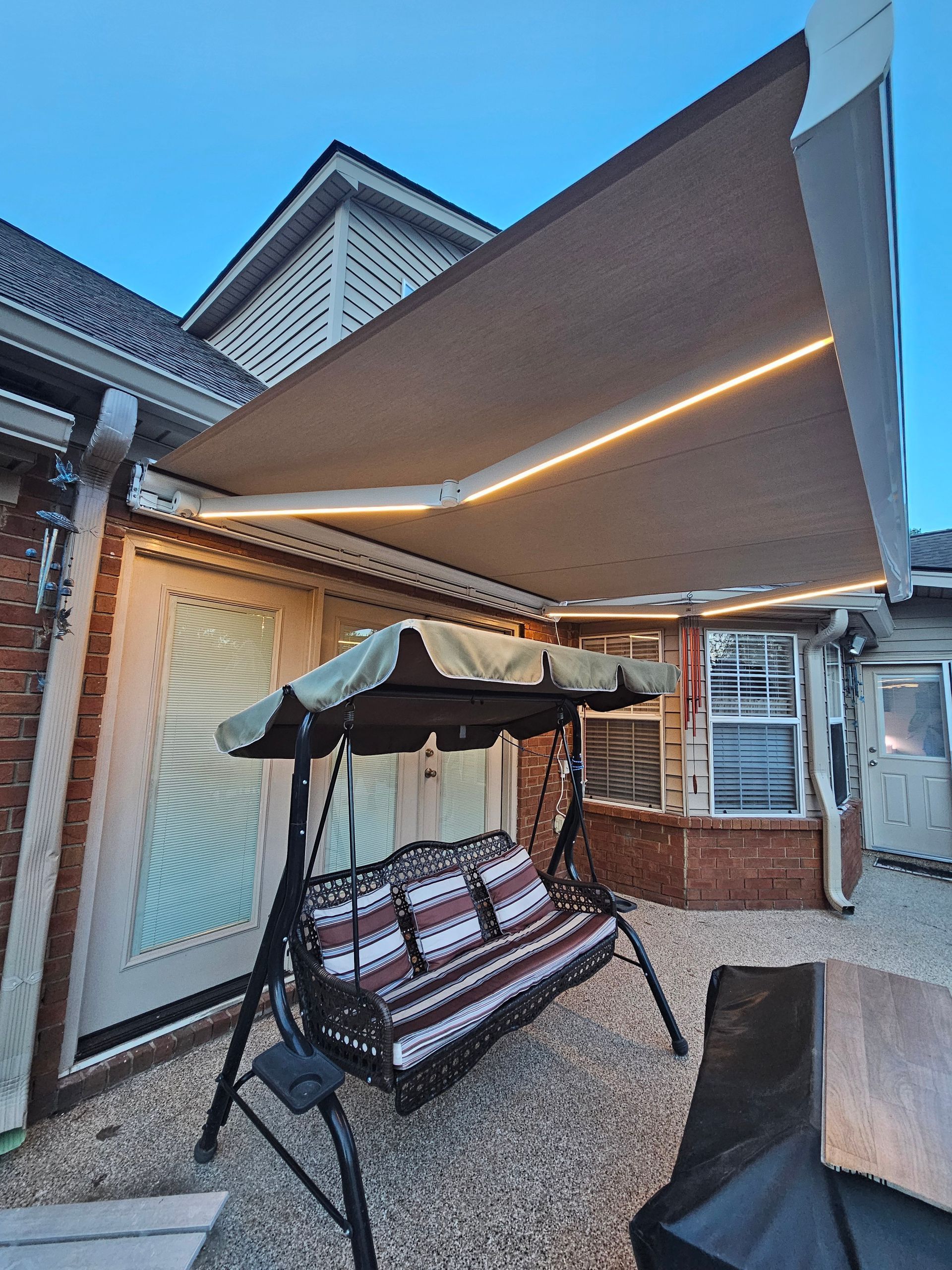 Backyard patio with a covered swing bench and retractable awning beside a house