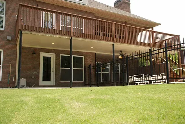 Backyard patio with two-story brick house, wooden deck, and fenced lawn