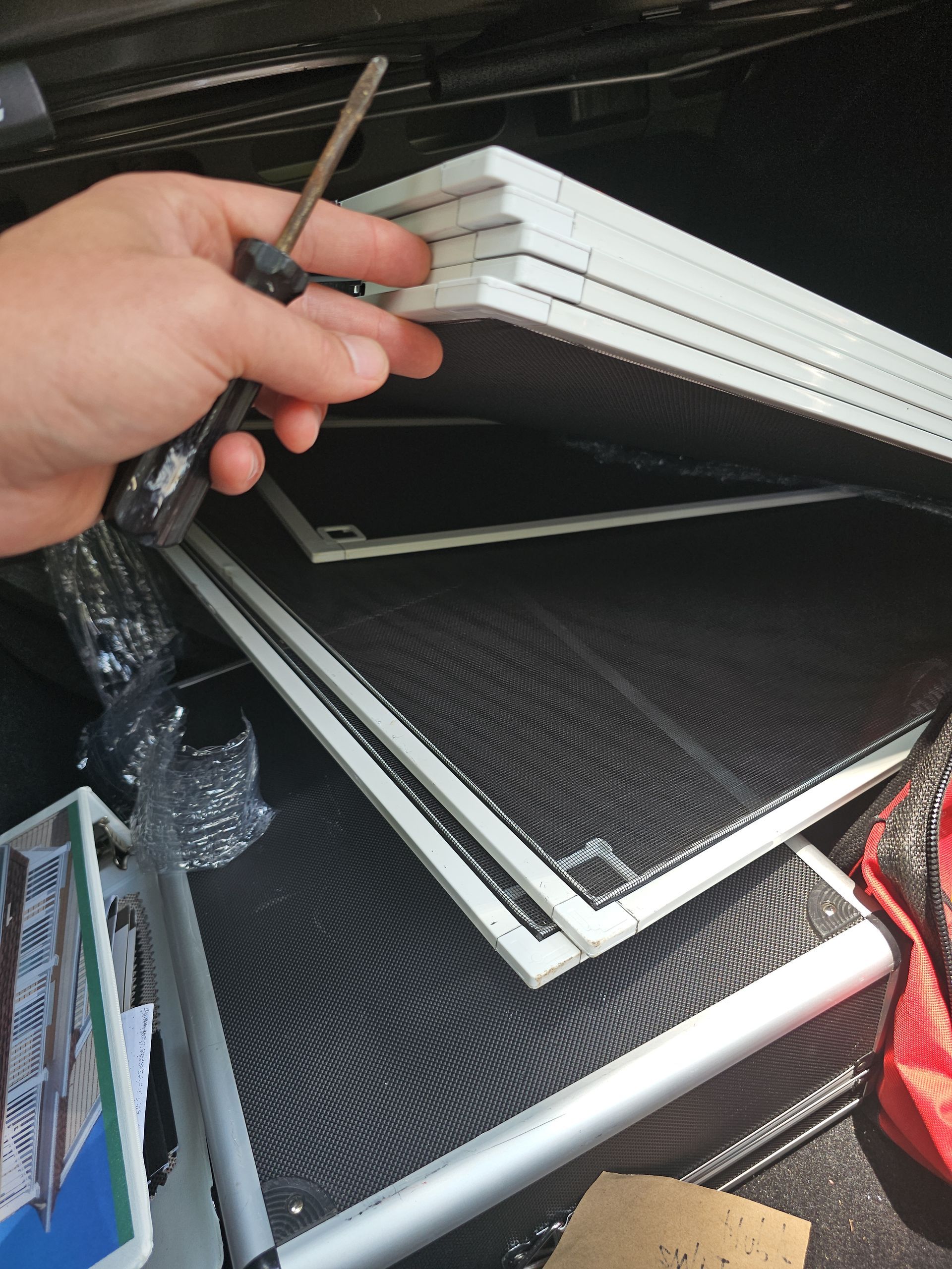 Hand holding a key over stacked white picture frames and black laptop covers in a storage bin