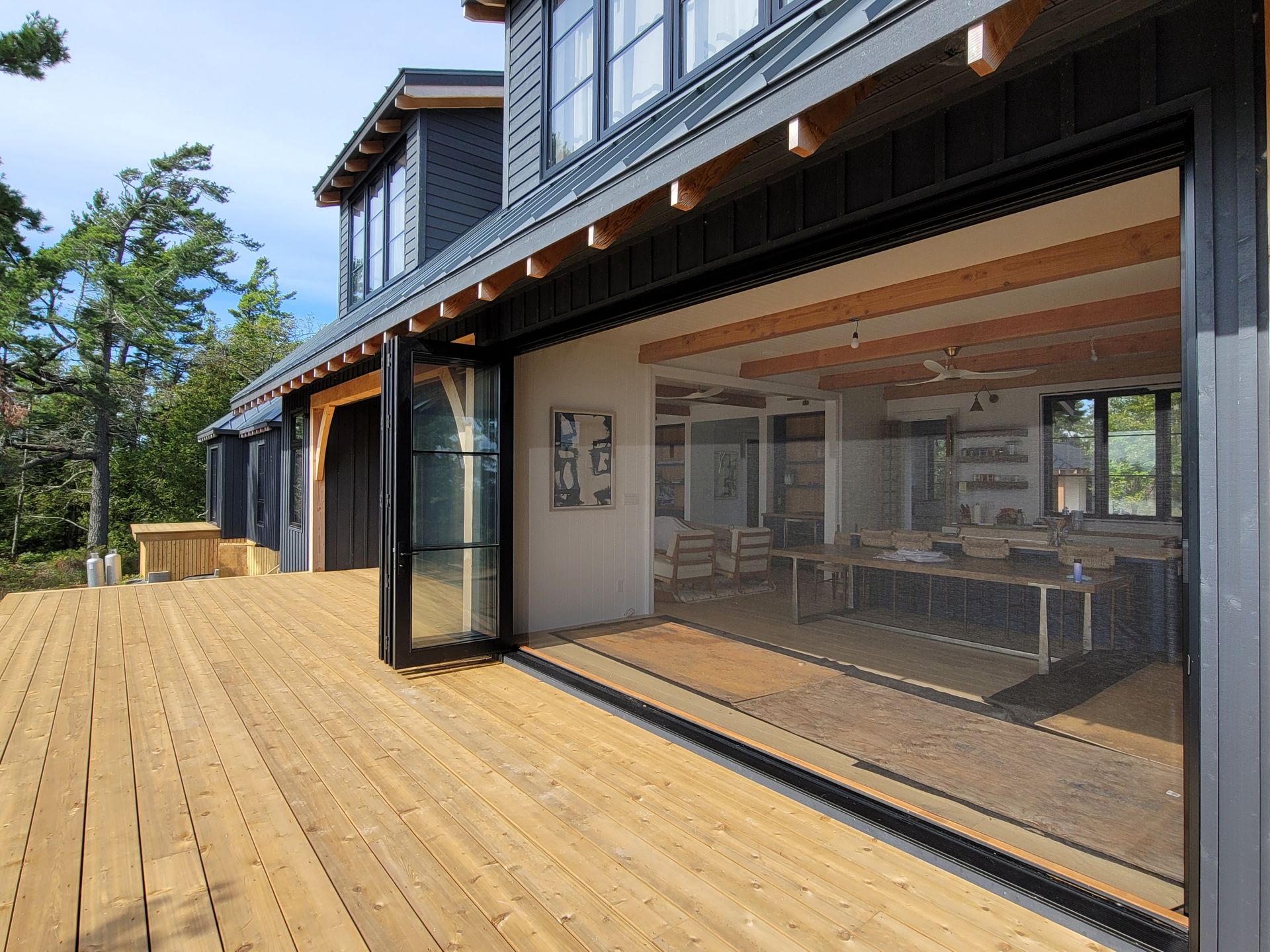 Modern house with a large glass wall opening onto a wide wooden deck and trees outside