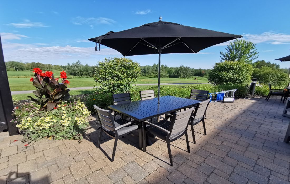 Patio dining set with black table, chairs, and umbrella overlooking a green garden and fields