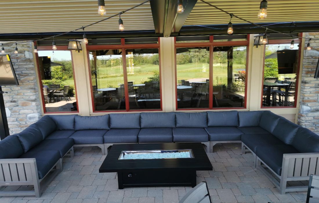 Covered outdoor patio with dark gray sectional sofa, black coffee table, and string lights overlooking greenery