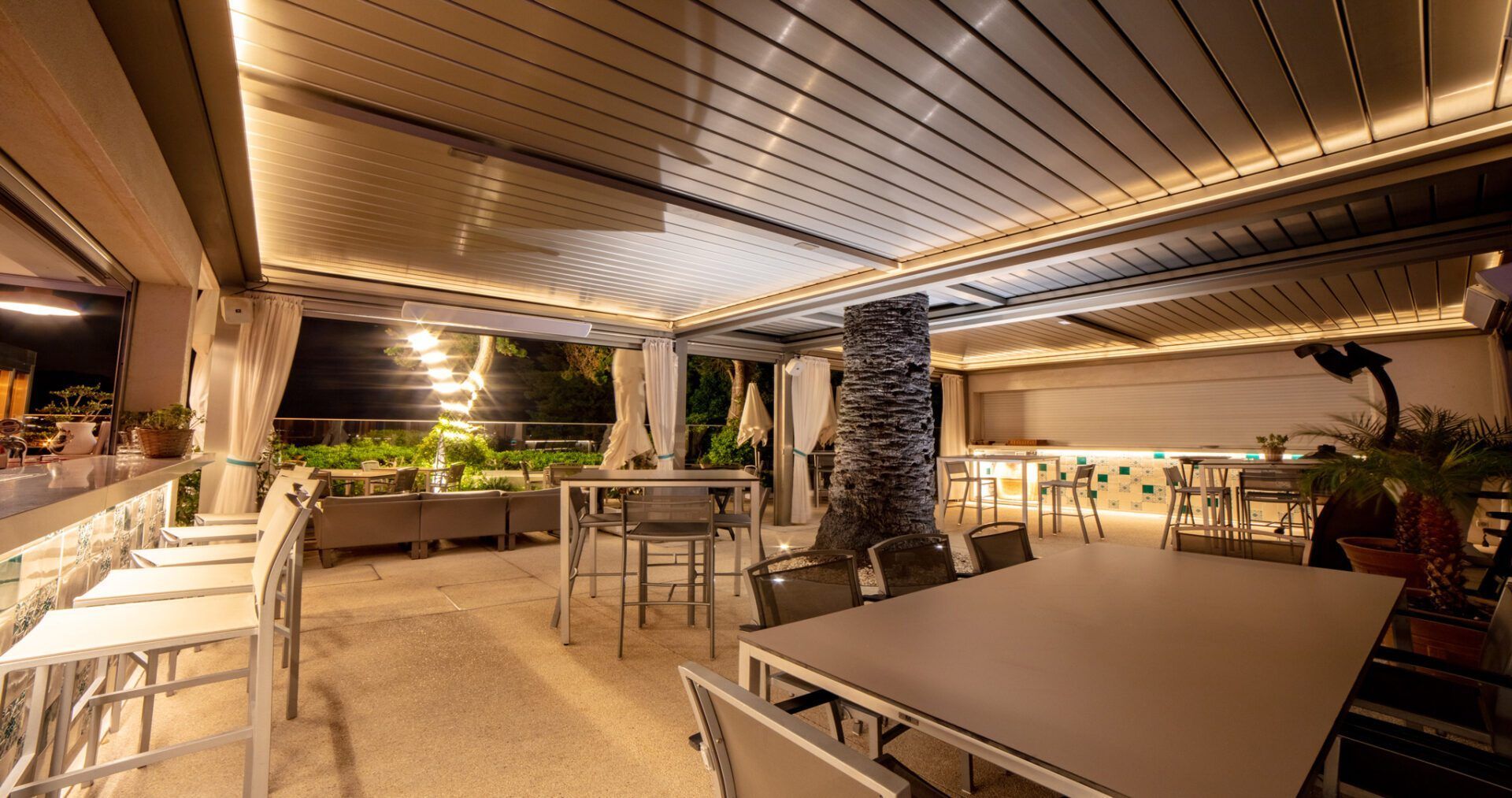 Covered outdoor restaurant patio with empty tables, chairs, and warm lighting at night