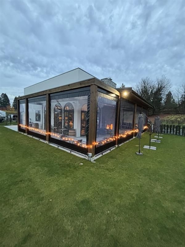 Modern glass-walled event tent with warm string lights on a grassy lawn at dusk