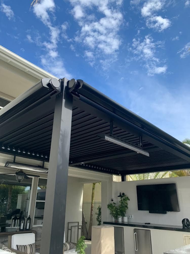 Covered outdoor patio with dark metal pergola, wall-mounted TV, and bright blue sky above