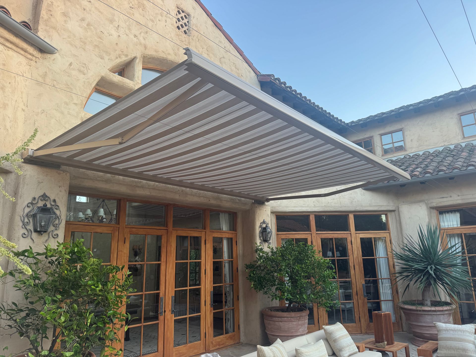 Patio with wooden French doors, potted plants, and a striped retractable awning on a stucco house