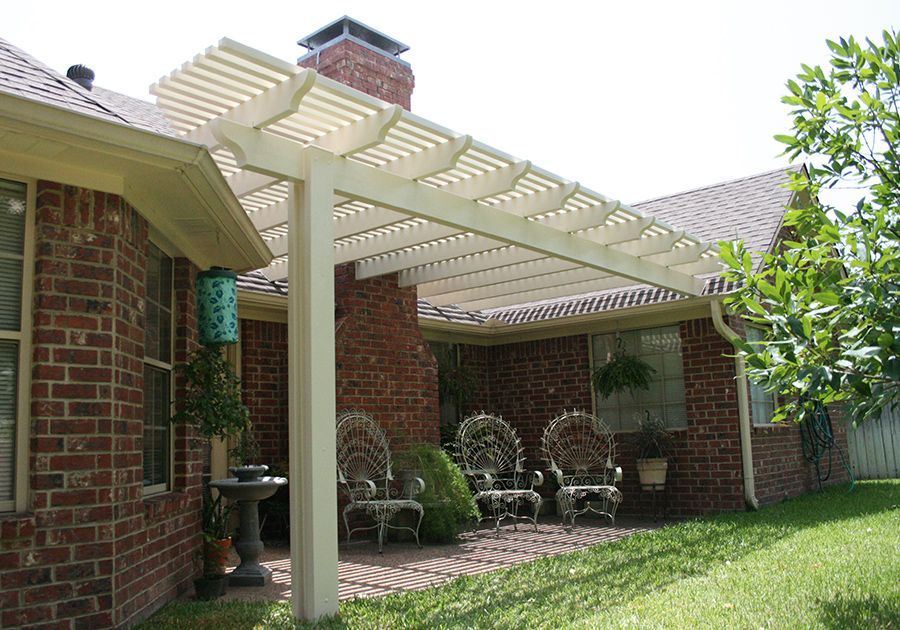 Brick patio with white pergola, outdoor chairs, and green lawn beside a house
