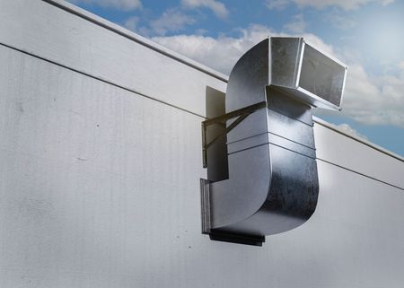 Metal ductwork attached to a building exterior, with a curved design, set against a cloudy sky.