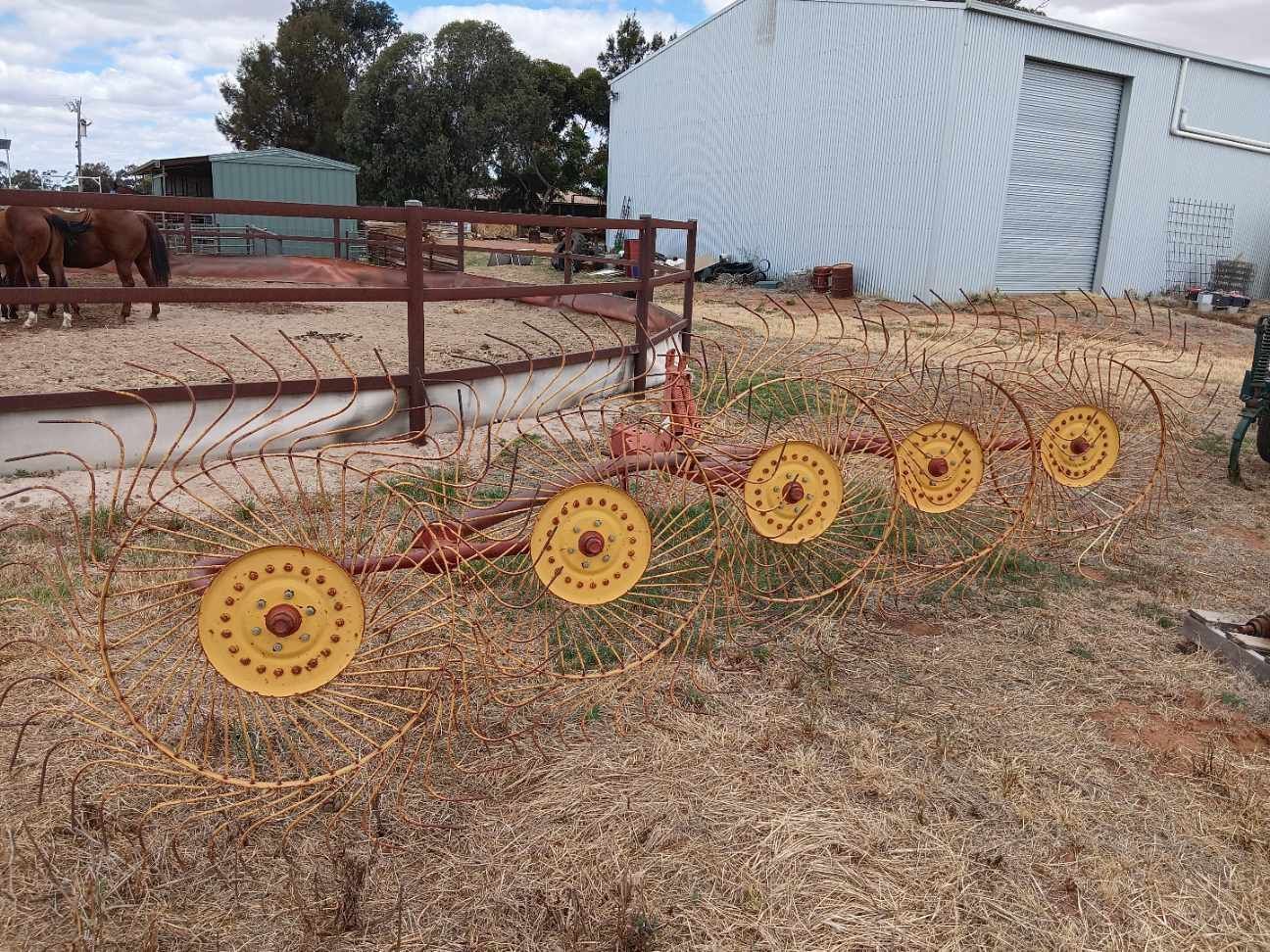 Yellow decorative wheel ornaments lined along a fence in a dry yard beside a white barn.