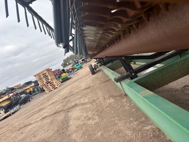 Tilted view of an industrial yard with stacked materials, machinery, and a large green conveyor or chute in the foreground