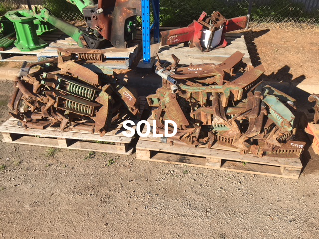 Pallets piled with rusty metal parts marked “SOLD” in a dusty outdoor yard