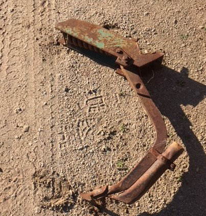 Rusty broken metal bracket on a rough concrete surface, lit by sunlight.