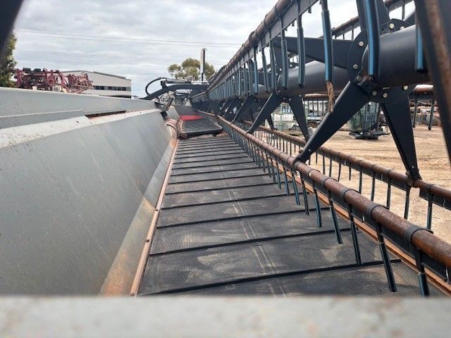 Industrial conveyor belt and machinery on a dusty outdoor site, viewed along the belt line.