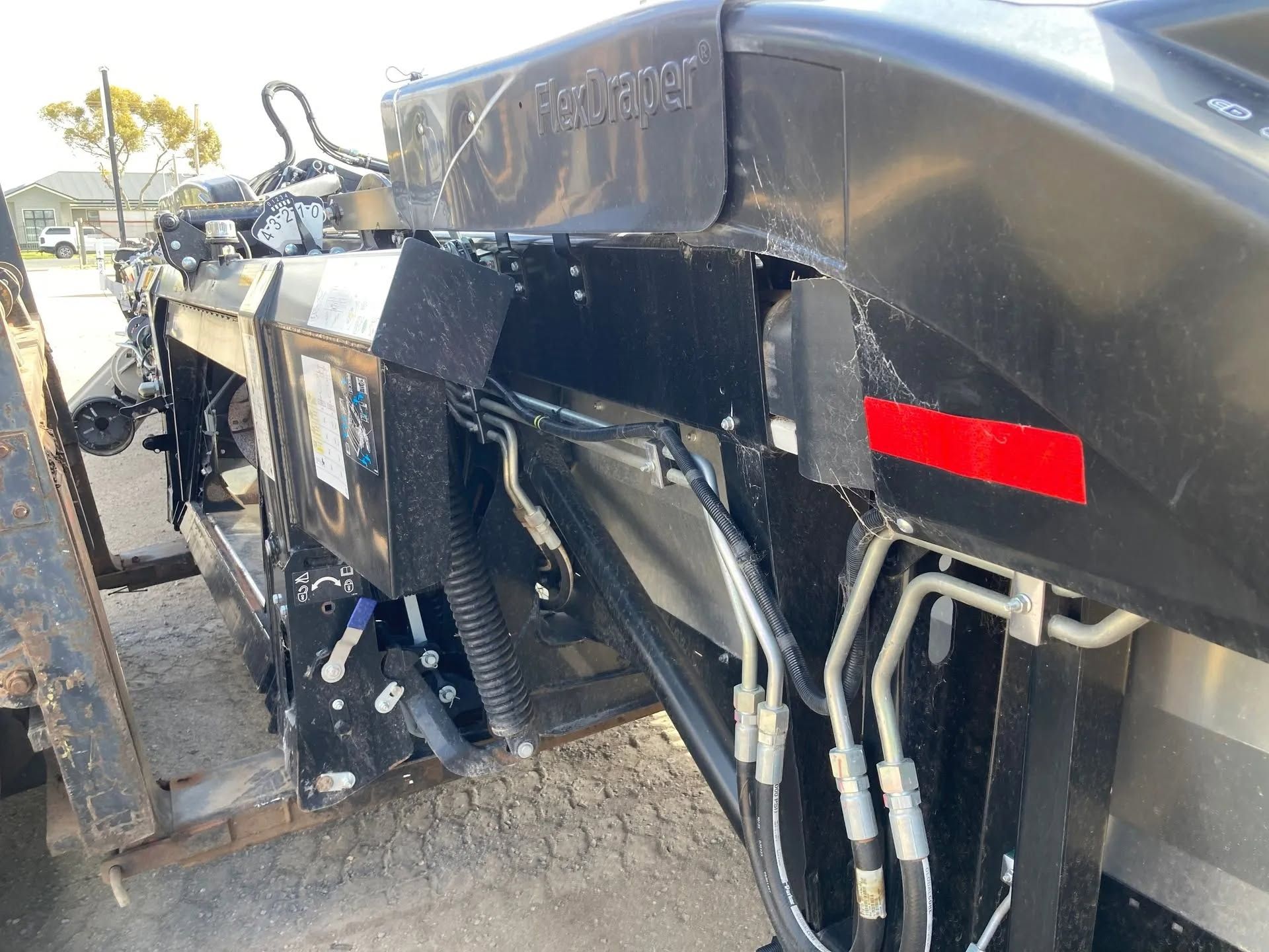 Damaged black heavy machinery with exposed parts and hydraulic hoses on a gravel surface