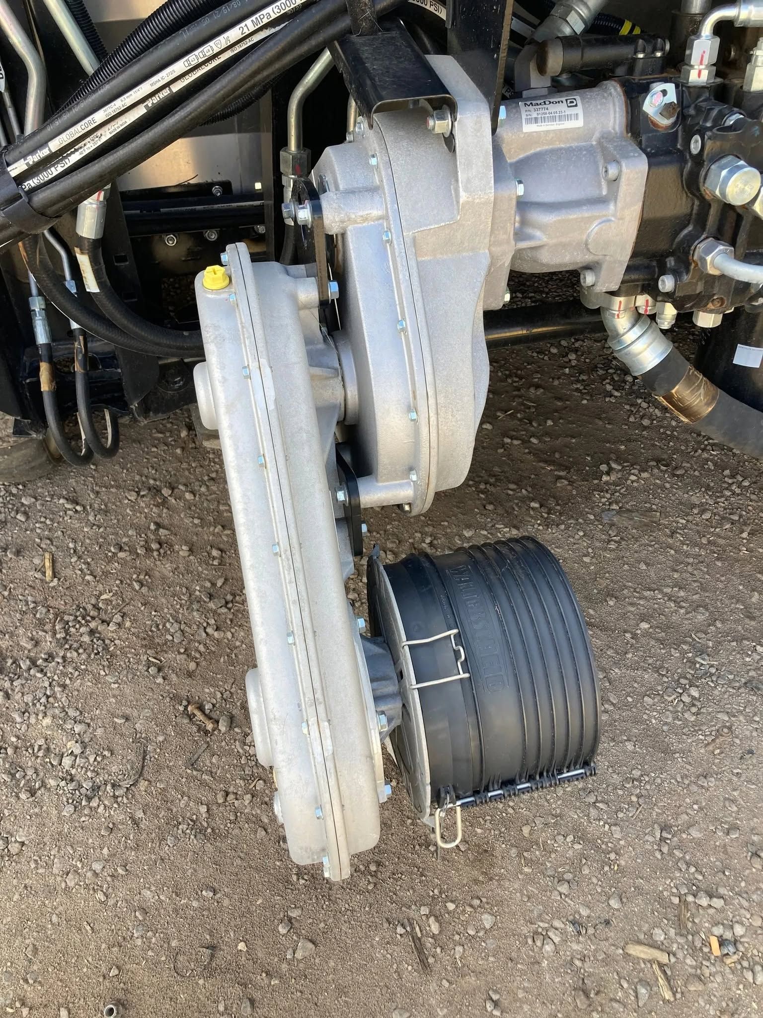 Close-up of industrial machinery with a white metal arm and black cylindrical component on gravel ground