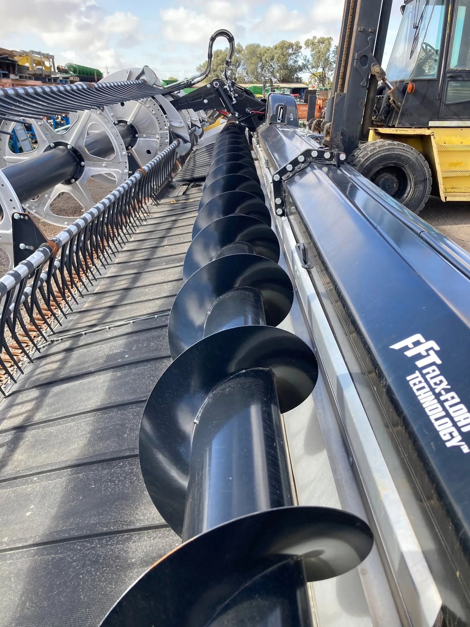 Agricultural machinery with long black augers on a trailer in a farm equipment yard