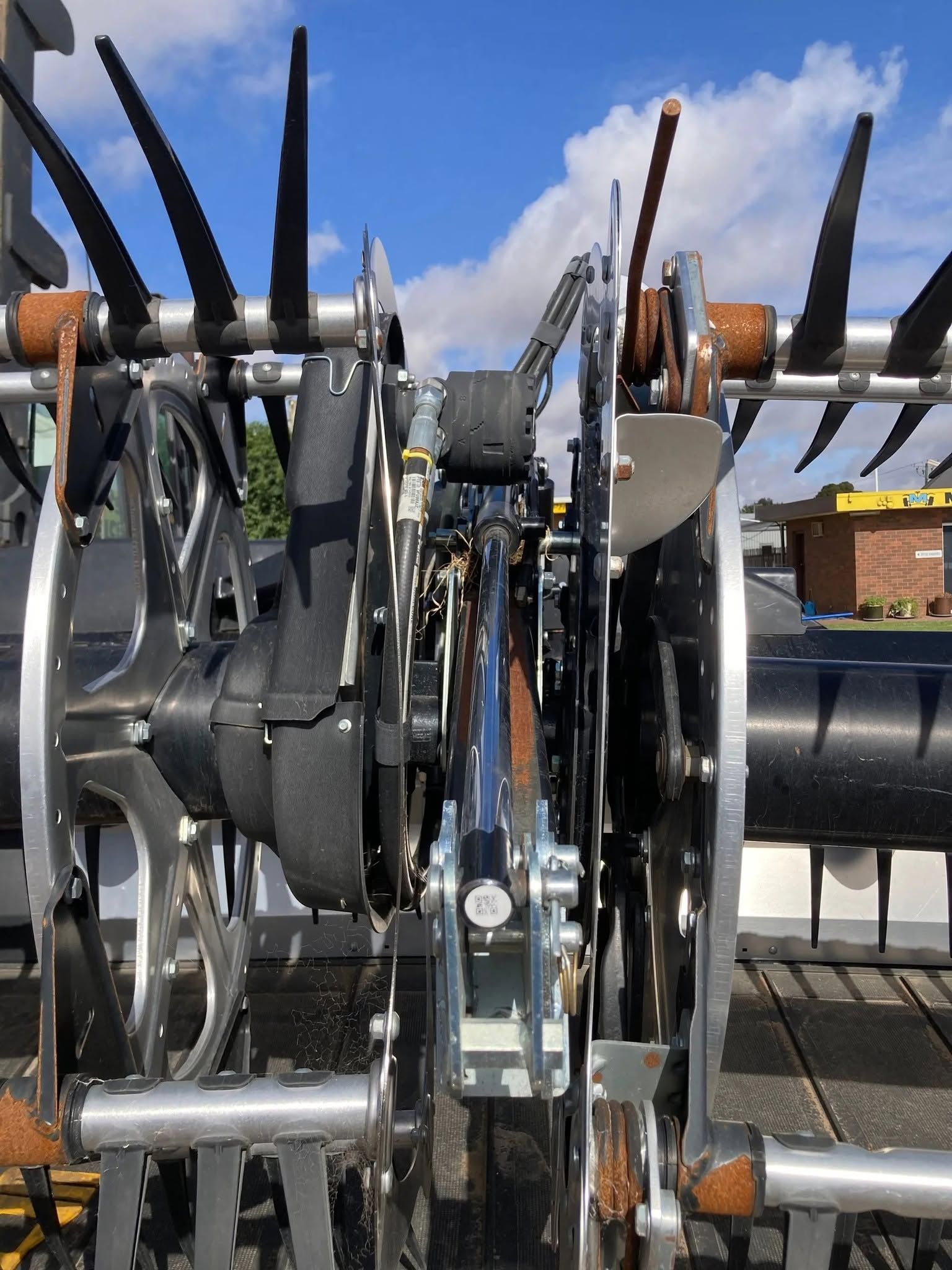 Close-up of a farm machine’s metal tines and rotating parts against a blue sky