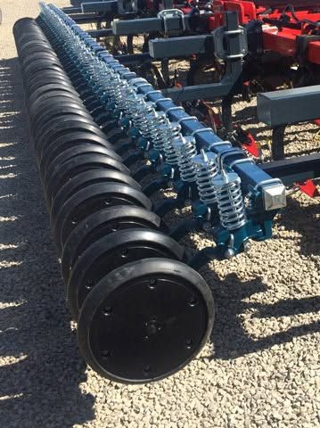 Row of black metal agricultural auger heads with blue springs, lined up on gravel outdoors.