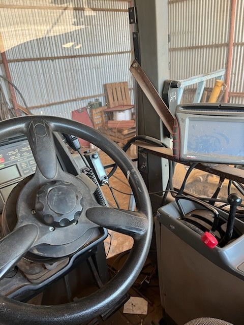 Inside a barn, a vintage vehicle cockpit with steering wheel, gear lever, and monitor on the dashboard