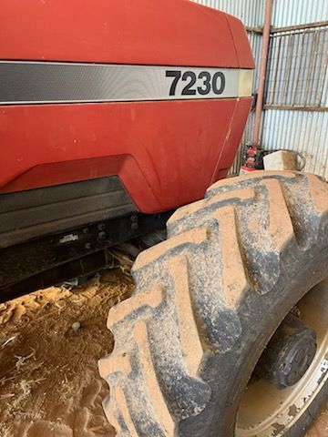 Red tractor with number 7230 and large muddy tire in a farm field