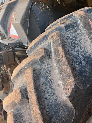 Close-up of a dusty tractor tire with deep treads, part of the vehicle visible in the background