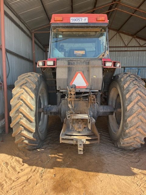 Front view of a red tractor with large muddy tires parked inside a shed