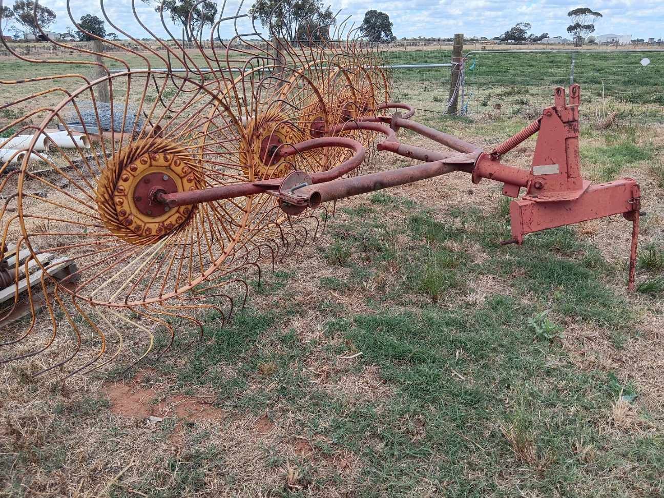 Rusty farm implement with wire-tine wheel in a grassy field
