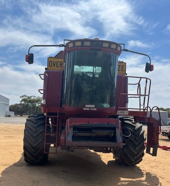 Front view of a large red agricultural harvester parked on a dirt lot under a blue sky.