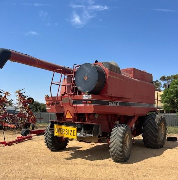 Red combine harvester with front auger and yellow “OVERSIZE” sign parked on a dusty farm road under blue sky