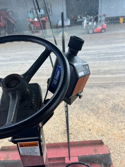 Forklift steering wheel and control panel in a warehouse, with equipment and floor in the background.