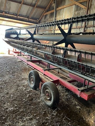 Large agricultural combine header on a red trailer inside a barn