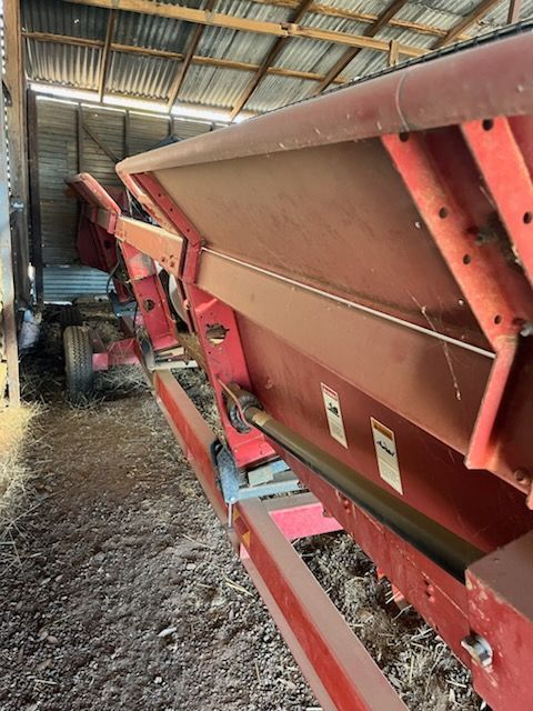 Red agricultural hopper conveyor inside a barn, with red metal frame and sloped bin