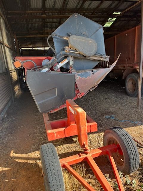 Orange farm equipment on a trailer inside a barn, with large metal bins and a tire visible.